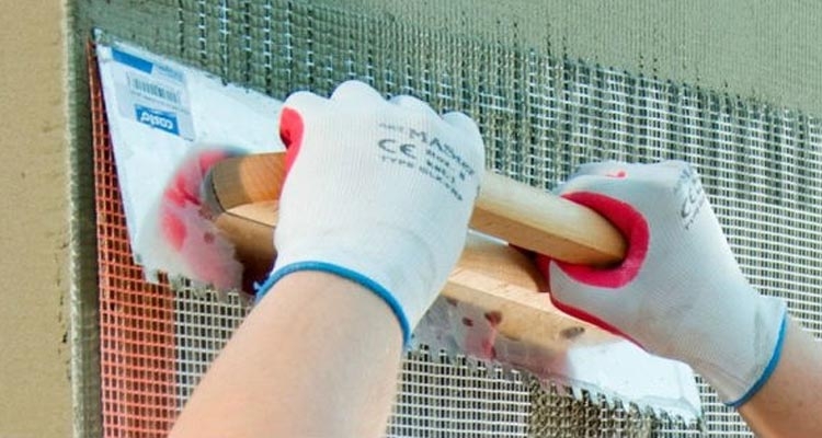 Zatapianie siatki w zaprawie podczas ocieplania domu. Fot. Baumit